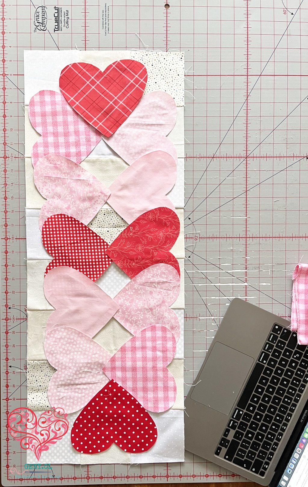 Doce corazones rojos y rosados preparados para las aplicaciones de Hearts Entwined sobre un fondo de patchwork neutro.