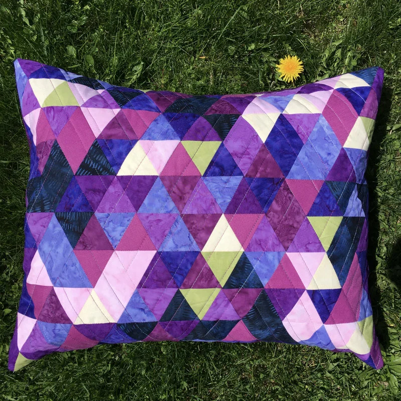 Hand Quilting con líneas de acolchado a mano sobre un quilt geométrico contemporáneo en tonos morados, violetas y verdes.