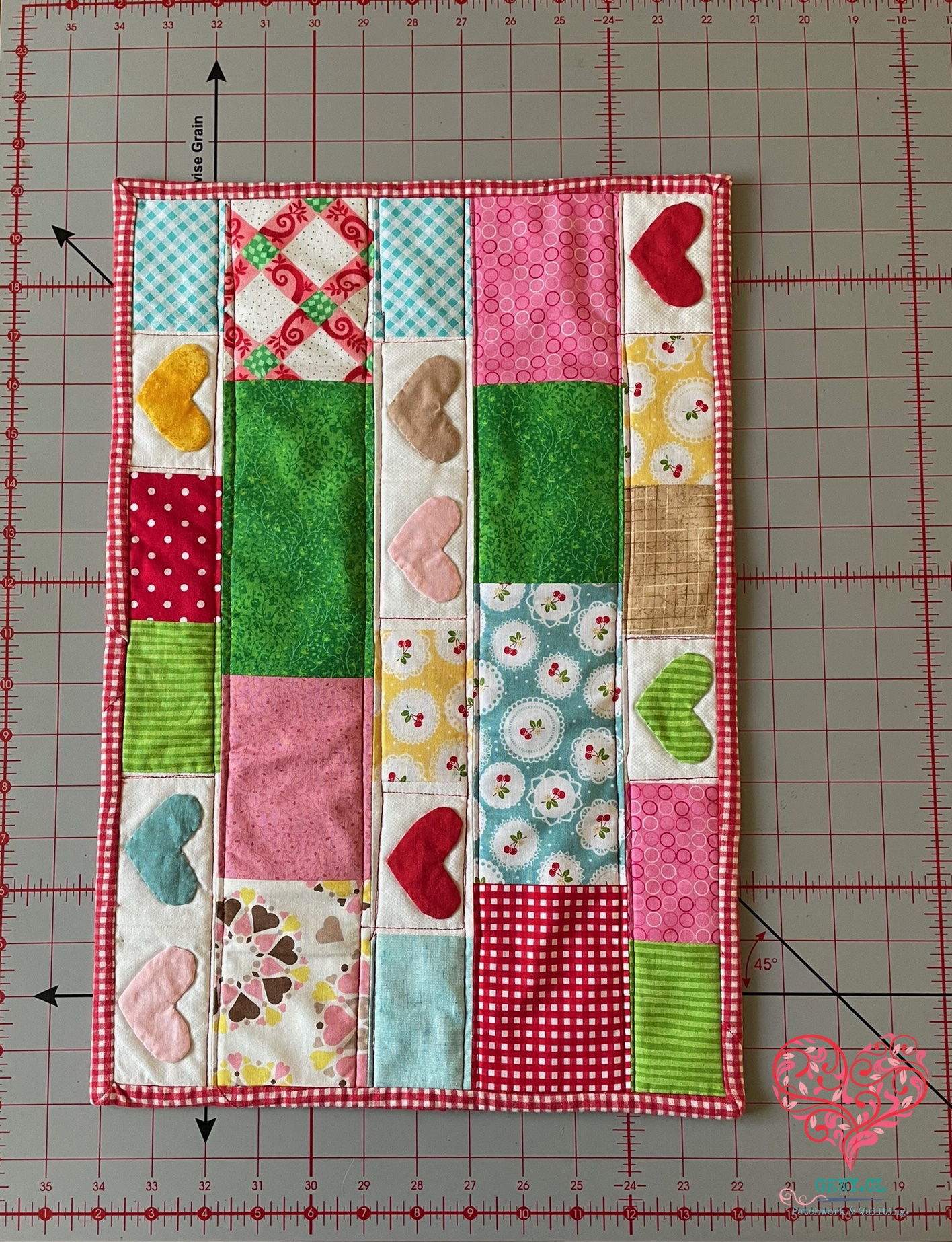 Mini quilt de patchwork con tiras de telas coloridas, corazones aplicados y acolchado discreto en las uniones.