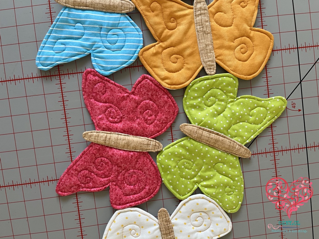 Detalle de espirales de free motion quilting sobre mariposas de patchwork fucsia, verde, naranja y calipso.