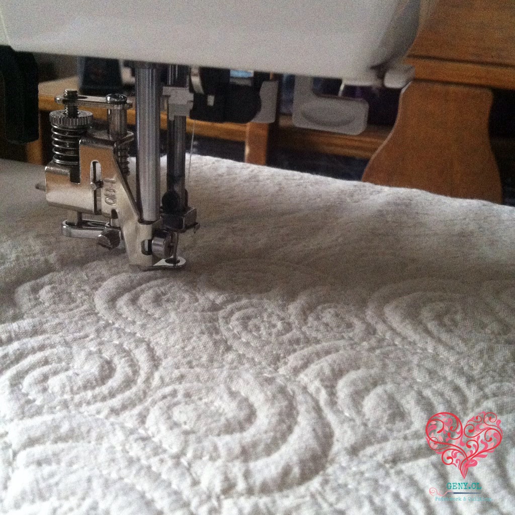 Prensatelas de máquina de coser sobre tela blanca acolchada con motivos de espirales y curvas en relieve.