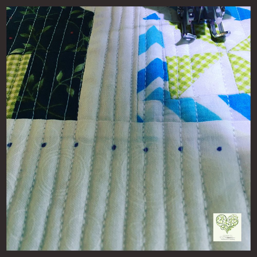 Detalle de acolchado a máquina con líneas rectas paralelas sobre un quilt de patchwork azul, verde y blanco.
