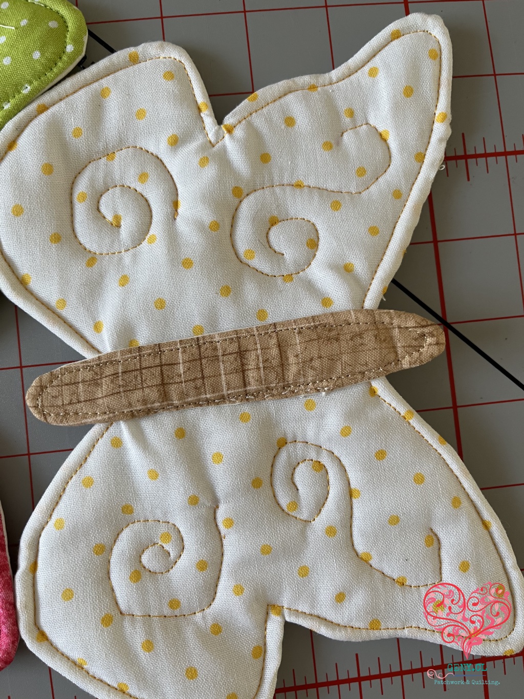 Primer plano de mariposa blanca con lunares amarillos, espirales acolchados con hilo dorado y cuerpo beige pespunteado.