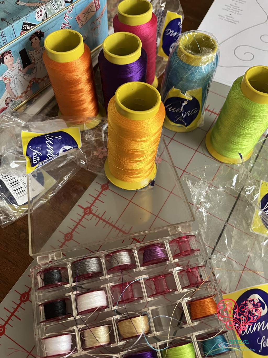 Conos de hilo trilobal Lumina de distintos colores, canillas y materiales de costura sobre una mesa de trabajo de patchwork.