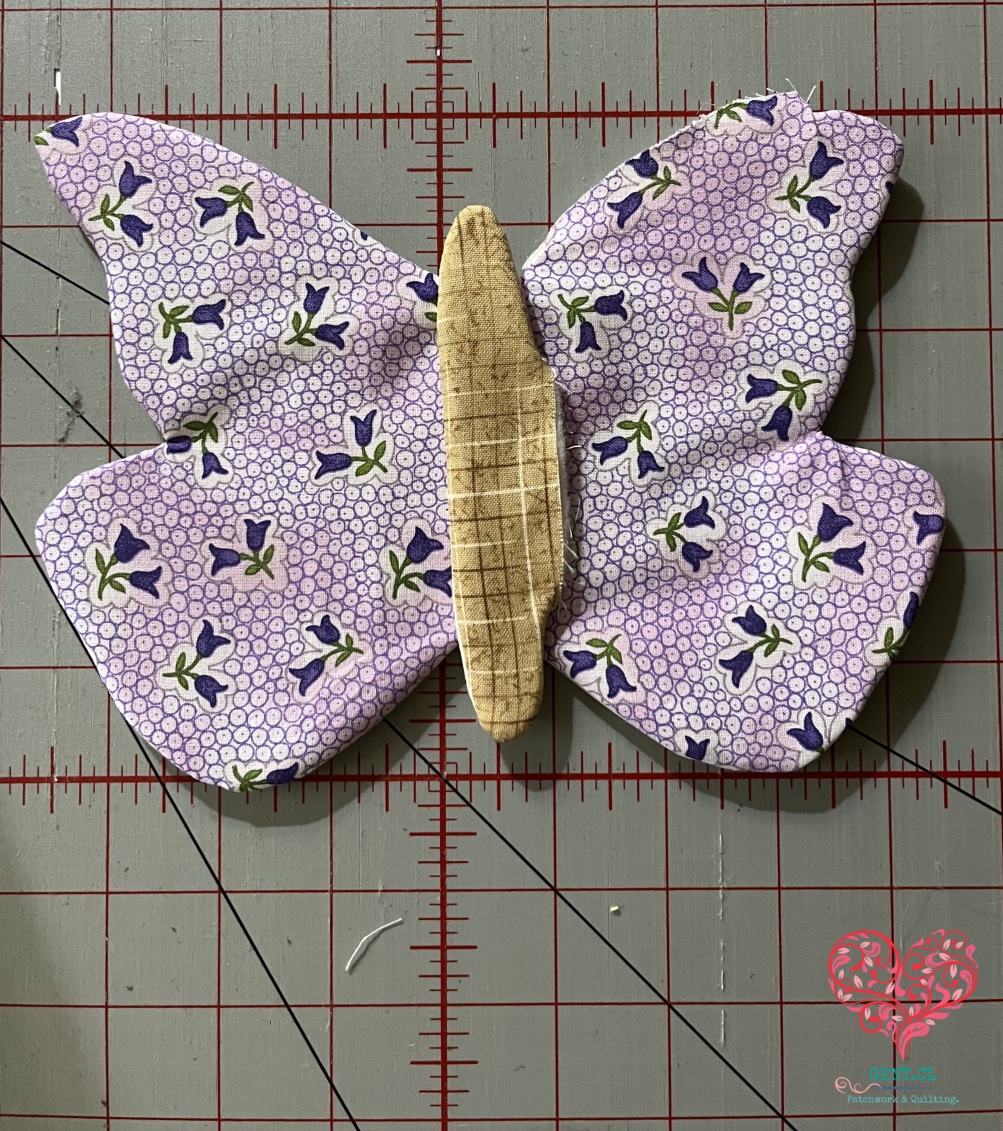 Mariposa de patchwork de tela lila con pequeñas flores moradas y cuerpo beige colocado sobre las alas.