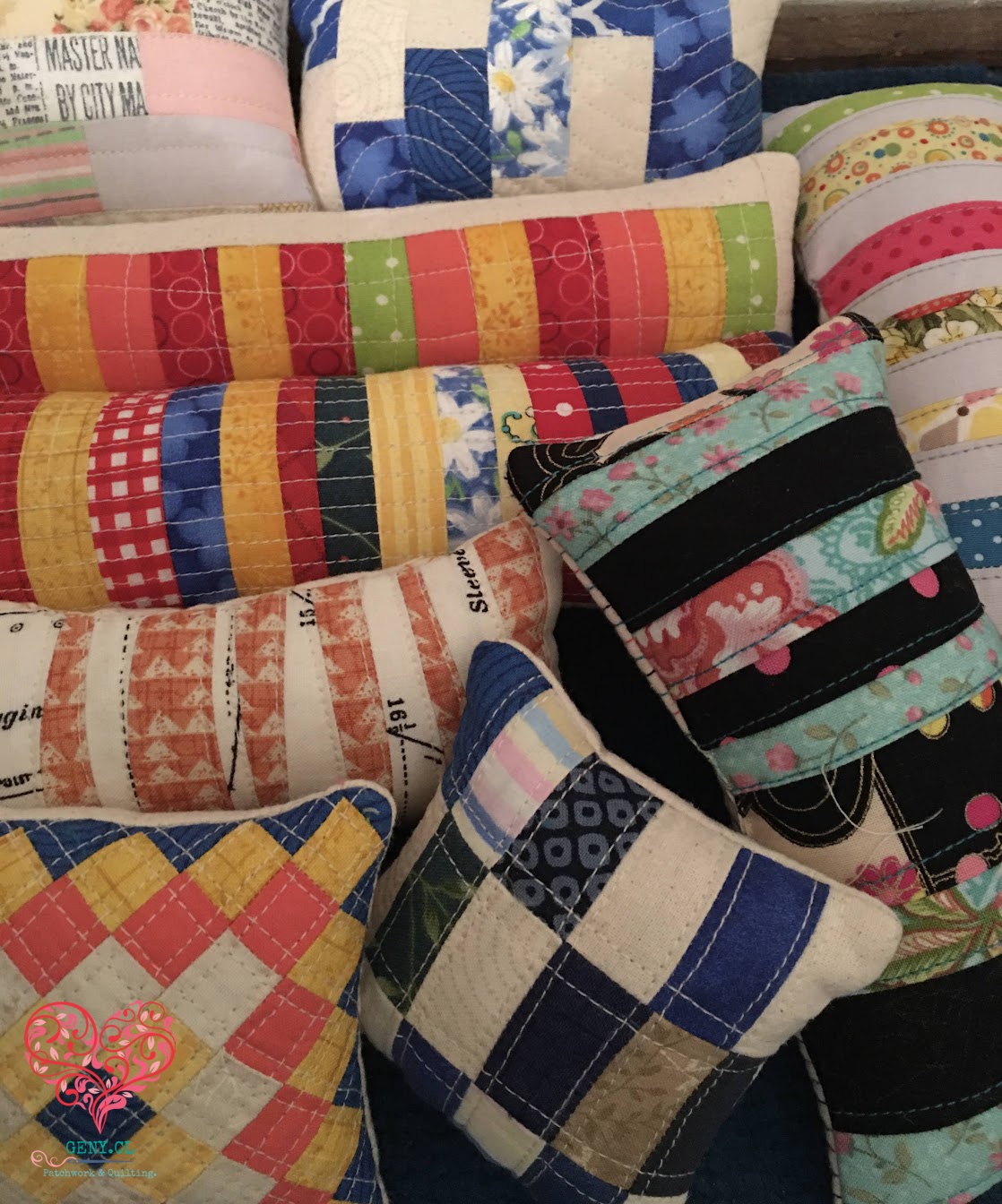 Colección de pequeños pin-cuchitos de patchwork confeccionados con telas de distintos colores y estampados.