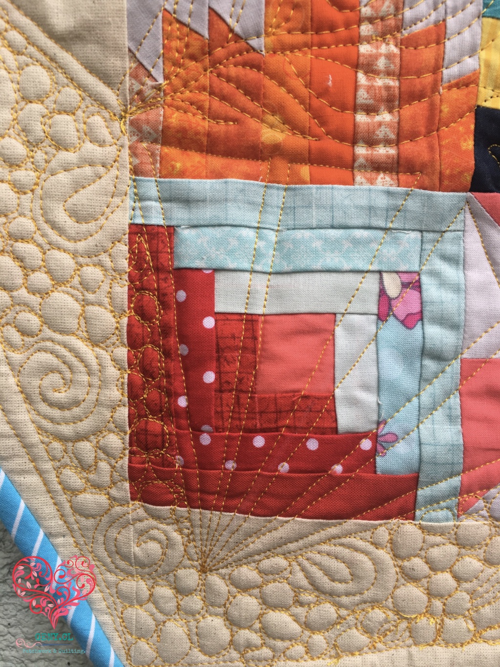 Detalle de quilting a máquina con hilo dorado formando flores, espirales y líneas sobre un quilt de patchwork