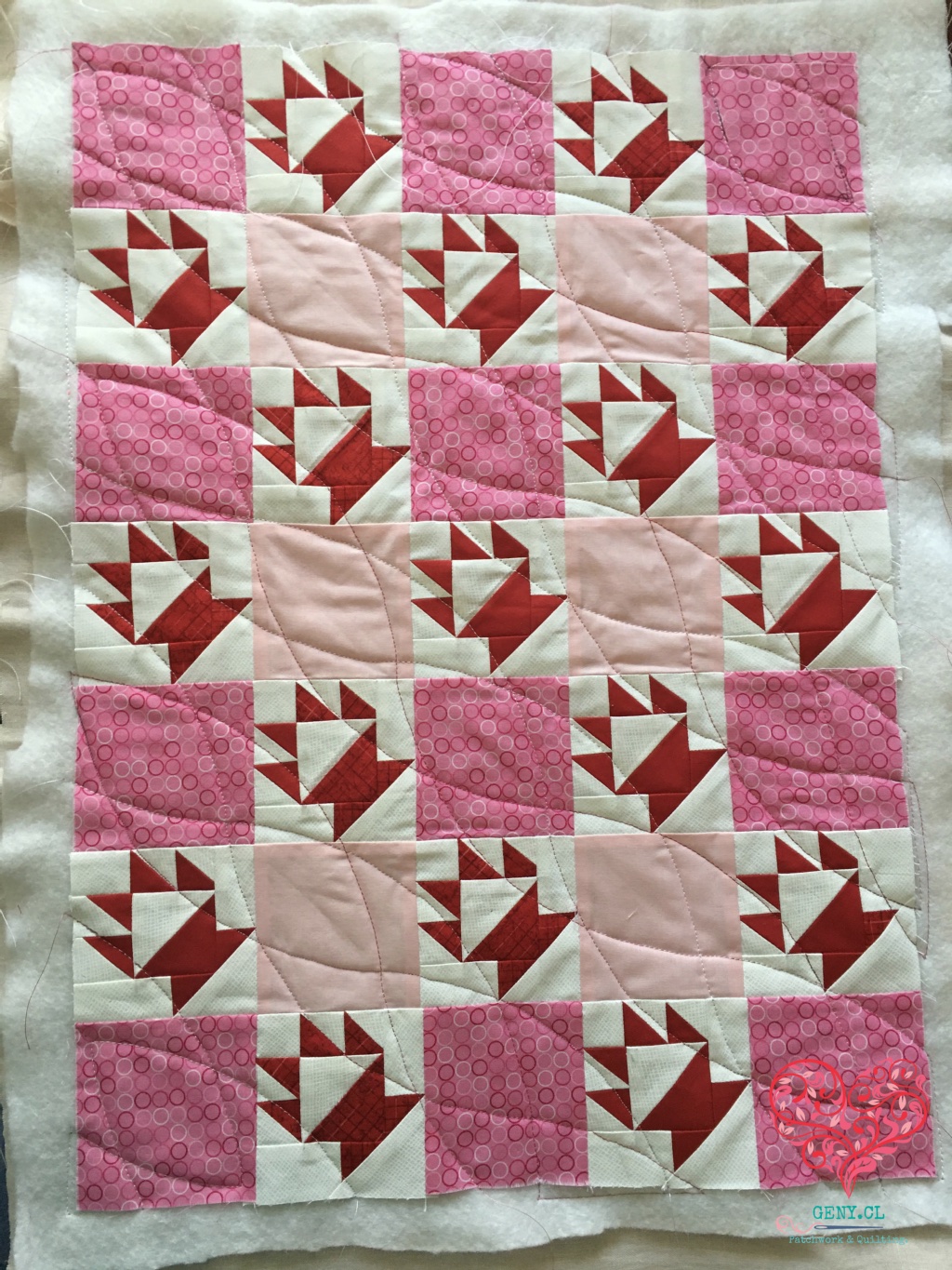 Quilt de patchwork rosado y rojo con acolchado curvo y punzonado visible alrededor del top.